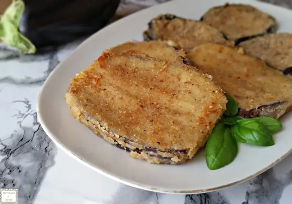 Fette dorate di cordon bleu di melanzane, impanate e fritte, servite su un piatto bianco con foglie di basilico fresco.