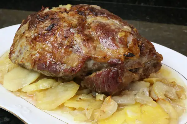 Cabezada de cerdo asada, jugosa y dorada, servida sobre patatas y cebolla caramelizada en un plato blanco.