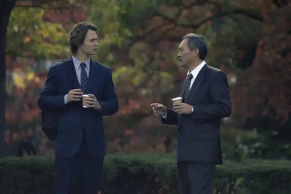 Zwei Männer in Anzügen, die Kaffee halten, diskutieren im Freien. Ein Mann ist jünger, der andere älter. Szene aus Tokyo Vice Staffel 2.