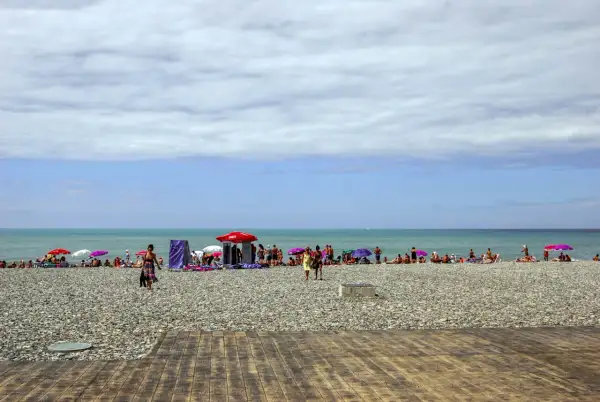 Tłum ludzi wypoczywa na kamienistej plaży w Batumi. Kolorowe parasole chronią przed słońcem.