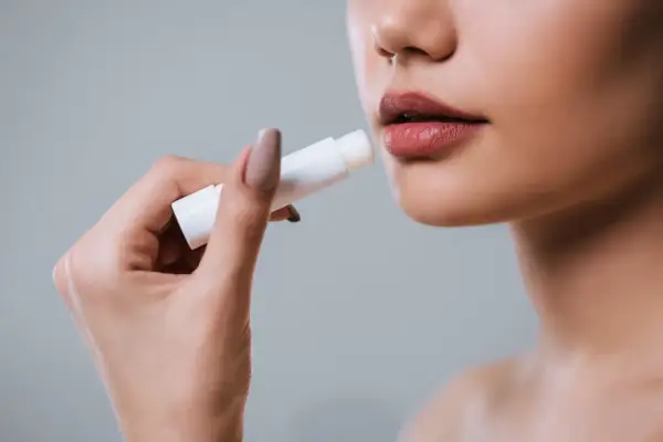Mano applica balsamo labbra per levigare le rughe, come un codice a barre che scompare.