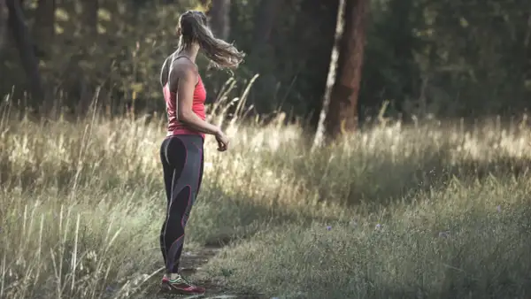 Frau im Laufoutfit im Wald. Sie genießt die Natur und die Ruhe, die das Joggen mit sich bringt.
