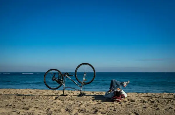 Odpoczynek po przejażdżce Velo Baltica. Rower na plaży, człowiek leży na piasku, patrząc na morze.