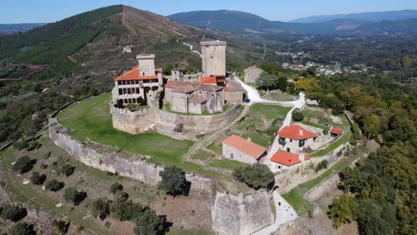 El imponente castillo de Monterrey se alza sobre una colina, rodeado de murallas de piedra y un paisaje verde.