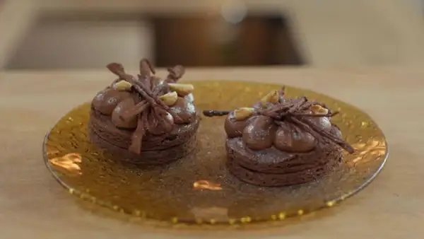 Dos bizcochos sin harina de chocolate, decorados con crema y avellanas, sobre un plato dorado.
