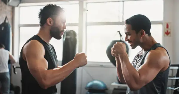 Two men in a gym, focused on their weight training for boxers. Punching bags and gym equipment are visible in the background.