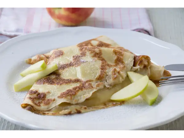 Zwei goldbraune Pfannkuchen mit Apfelmus gefüllt, garniert mit Apfelspalten und Puderzucker.
