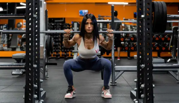Donna determinata esegue squat con bilanciere in palestra. Gli squat fanno dimagrire e scolpiscono il corpo, un passo alla volta.