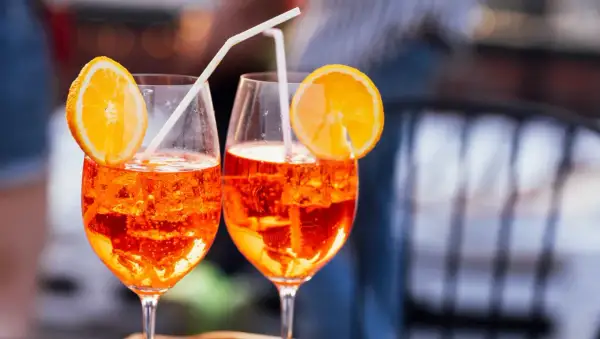 Dos Aperol Spritz refrescantes, con rodajas de naranja y pajitas, evocan el aperitivo italiano y su aperol spritz origen.