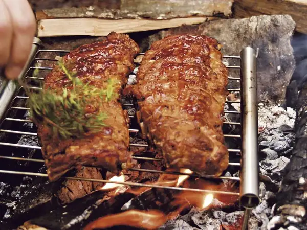 Två saftiga spareribs grillas över öppen eld. En hand lägger på en kvist rosmarin för extra smak.