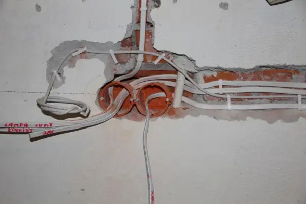 Rozpoczęta wymiana instalacji elektrycznej: widoczne puszki, przewody i fragmenty ceglanej ściany.