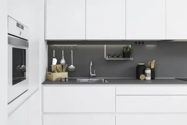 Moderna cocina blanca y gris con electrodomésticos integrados, fregadero de acero inoxidable y utensilios de cocina colgados.