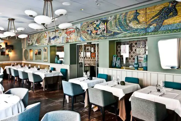 Interni eleganti di un ristorante, con tavoli apparecchiati e un grande mosaico marino sul muro. Un luogo ideale per scoprire i migliori ristoranti di pesce a Milano.