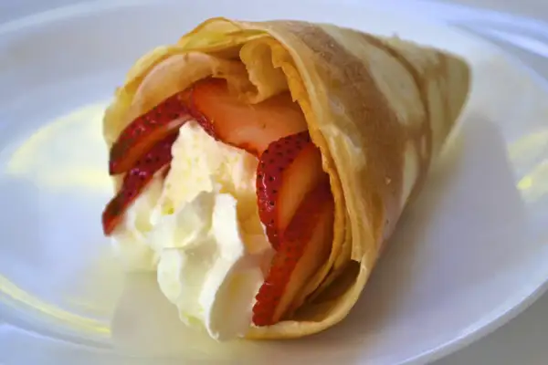 Délicieuse crêpe japonaise moelleuse garnie de fraises fraîches et de crème fouettée, servie sur une assiette blanche.
