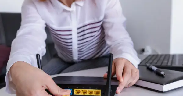Ręce podłączają kabel do routera, pokazując, jak wejść na router. Obok leży laptop i notatnik.