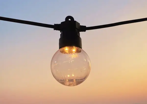 Guirlande lumineuse extérieure, une ampoule sphérique éclairée sur fond de ciel crépusculaire. La définition IP protection garantit sa résistance.