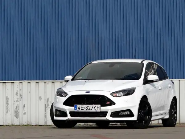 Biały Ford Focus ST z silnikiem 2.0 TDCI, zaparkowany przed niebieską, falistą ścianą.