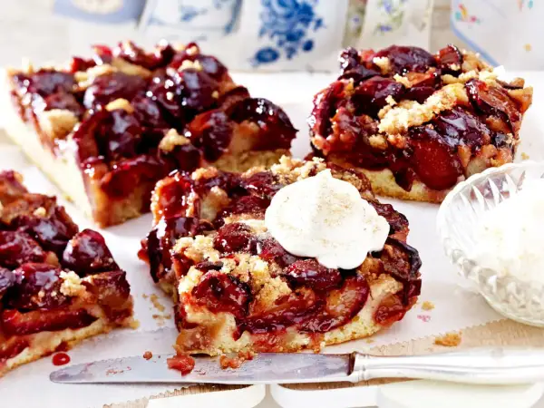 Saftige Pflaumenstücke auf einem lockeren Teig, bestreut mit Streuseln. Ein Stück gesunder Pflaumenkuchen mit einem Klecks Sahne.