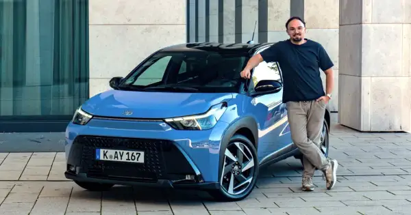Mężczyzna opiera się o niebieską Toyotę Aygo X Hybrid.