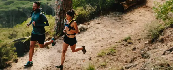 Deux coureurs s'entraînent sur un sentier de montagne, profitant d'un entraînement fractionné trail dans un paysage verdoyant.