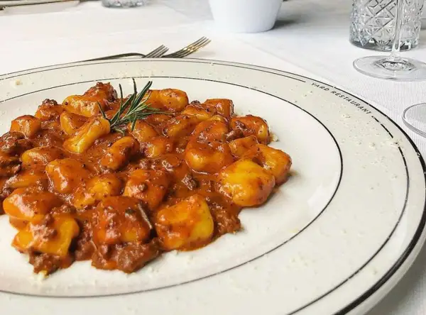 Gnocchi al ragù, un classico tra i piatti tipici maceratesi, serviti su un piatto bianco con rosmarino fresco.