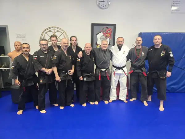 En grupp män i svarta och vita dräkter poserar på en blå matta. De är en del av en kenpo karate-klubb.