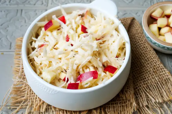 Frischer sellerie salat mit roten Apfelstücken, garniert mit schwarzem Pfeffer, serviert in einer weißen Schüssel auf Jute.