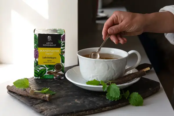 En hand rör om i en kopp te. Bredvid står en ask med Skandinavisk Twist Lakritstäppa, som ger te smak.