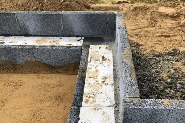Grunden byggs med lecablock. Sand och grus syns runt den pågående murningen.