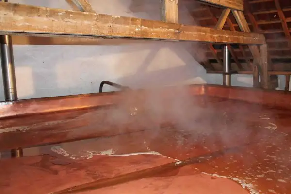 Vapore sale da una grande vasca di rame in una lambiek fabriek. La luce illumina il processo di produzione della birra.