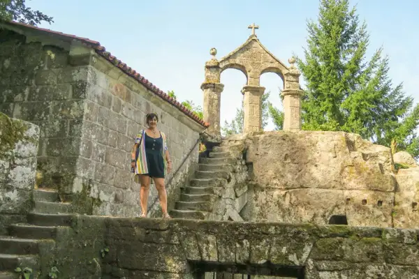 Mujer posa frente a la entrada del monasterio de San Pedro de Rocas, con su arquitectura de piedra y escalinata antigua.