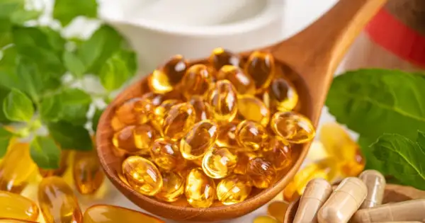 Łyżka pełna kapsułek z płynnym złotem – to suplementacja omega 3. Obok zielone liście i inne suplementy.