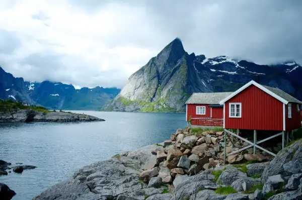 Två röda stugor vid en sjö i Norge, med dramatiska berg i bakgrunden. Perfekt för en vandring i Norge.