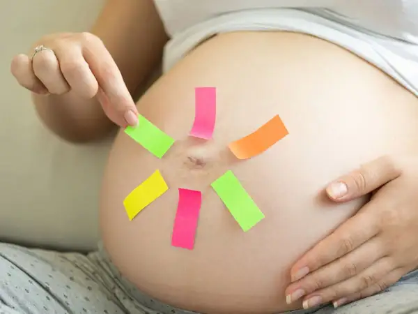 Une femme enceinte place des post-it colorés sur son ventre, peut-être pour choisir un prénom en P pour son bébé.