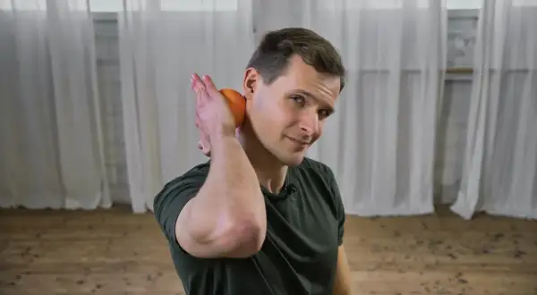 Mann lockert Nackenmuskulatur mit einer Orange.