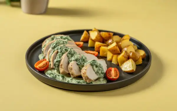Pokrojona pierś z kurczaka ze szpinakiem w sosie śmietanowym, podana z pieczonymi ziemniakami i pomidorkami koktajlowymi.