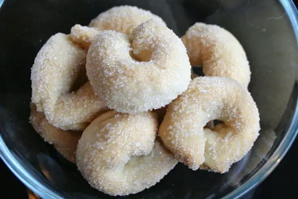 Un gruppo di taralli dolci, ricoperti di zucchero cristallino, in una ciotola di vetro.