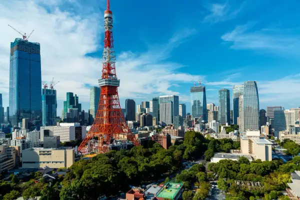 Tokio Tower góruje nad nowoczesnym miastem z wieżowcami w budowie i zielonymi drzewami.