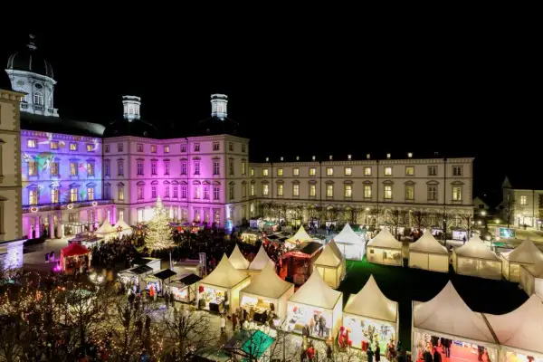 Festlicher weihnachtsmarkt schloss bensberg mit beleuchtetem Baum, bunten Lichtern und vielen Besuchern in Zelten.