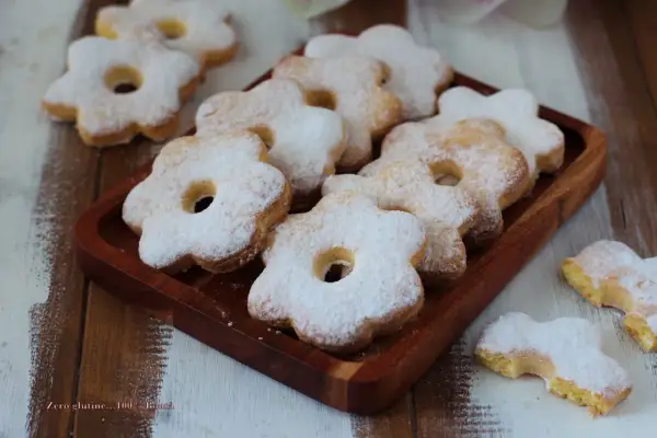 Deliziosi dolci solo tuorli benedetta, a forma di fiore, cosparsi di zucchero a velo su un vassoio di legno.