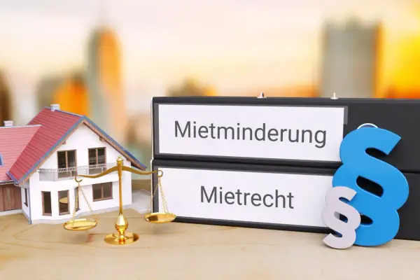 Hausmodelle, Waage der Gerechtigkeit und Ordner mit "Mietminderung" und "Mietrecht" – ein Symbol für die Bewertung von Wasserschäden.