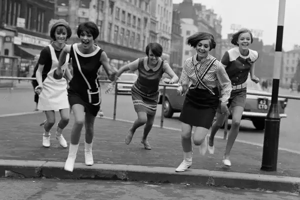 Cinco chicas con minivestidos y botas, al estilo de Mary Quant, corren alegres por la calle.