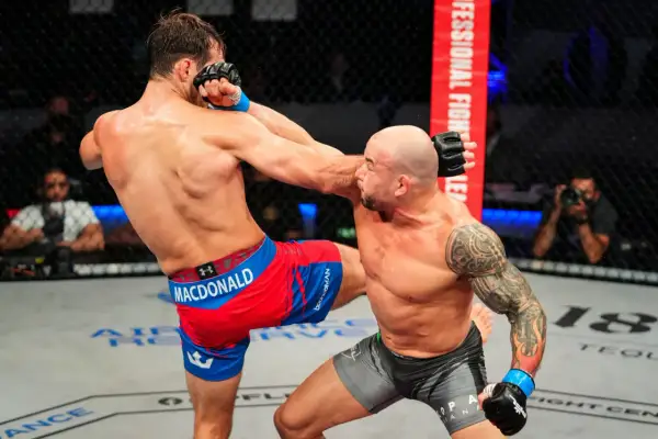En MMA-fighter med tatueringar på armen, likt Gleison Tibau, tar emot en spark i ansiktet.