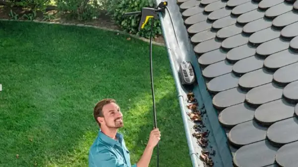 Hombre sonriente usando un accesorio para limpiar canalones altos con una hidrolimpiadora.