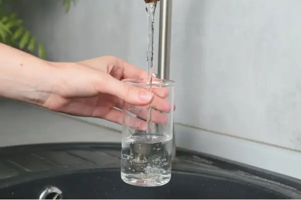 Main tenant une éprouvette graduée sous un robinet, elle se remplit d'eau. La mesure du TDS, signification de la teneur en solides dissous, est peut-être en cours.