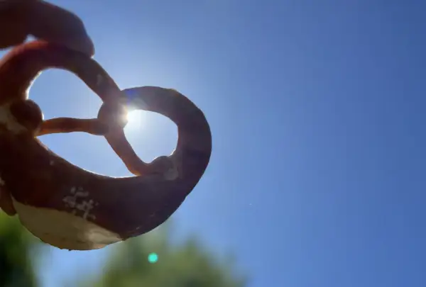 Ein Brezel wird gegen die Sonne gehalten. Woher kommen Brezeln? Aus dem Teig, der zu dieser Form geknetet wird.