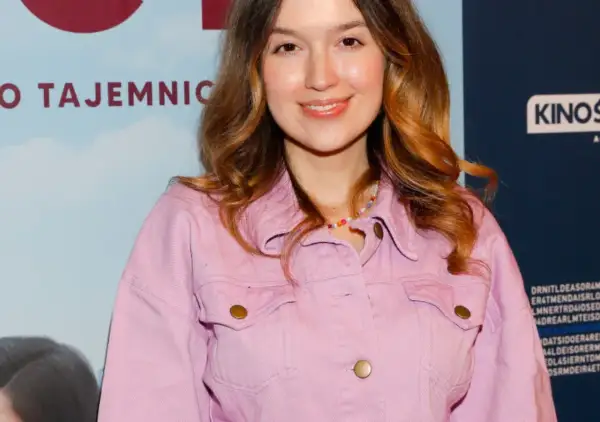 Uśmiechnięta Natalia Sisik w różowej kurtce, z kolorowym naszyjnikiem.
