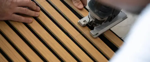 Mani che guidano un seghetto alternativo per tagliare pannelli fonoassorbenti in legno.