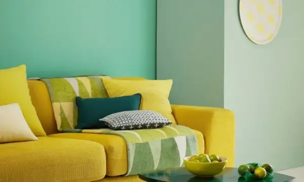 Divano giallo acceso con cuscini colorati e una coperta con motivi geometrici in **colore verde**. Sul tavolino, una ciotola di lime.