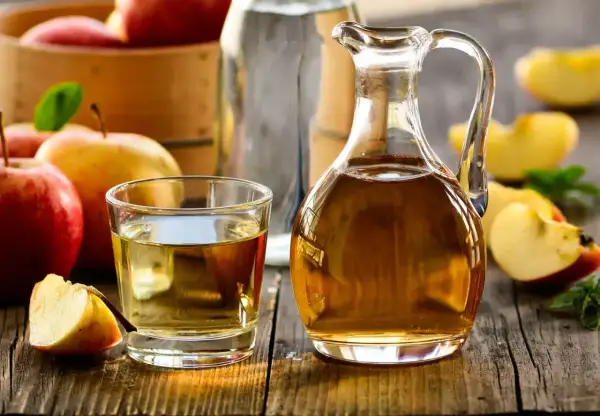Aceto di mele in caraffa e bicchiere, con mele fresche. Un rimedio naturale per un bucato morbido.